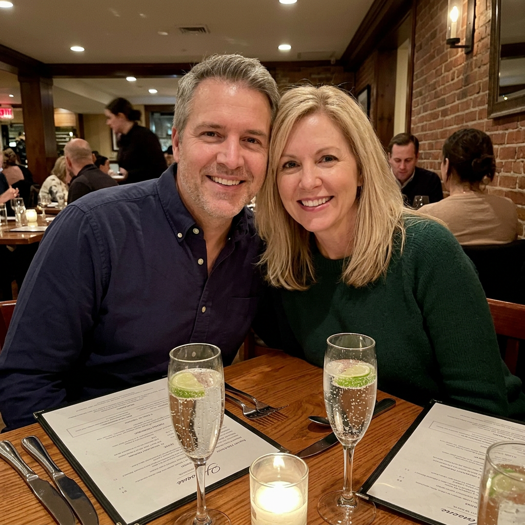 Fletcher and Maggie at a restaurant table, both smiling, sparkling water in front of him